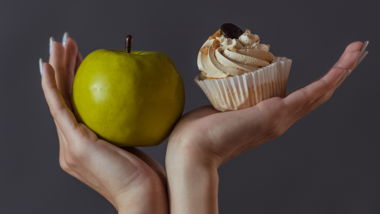 Hand choosing between a healthy apple and a cupcake representing self-control and food choices for diabetes management