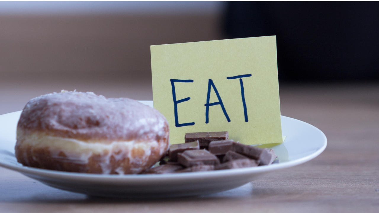 Doughnut and chocolate on a plate with a label saying “eat,” symbolising emotional cravings
