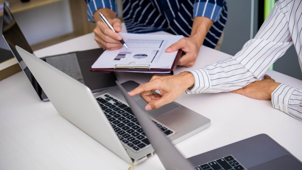 Two people reviewing a chart on a laptop and clipboard to track blood sugar and health progress for reversing type 2 diabetes after 50